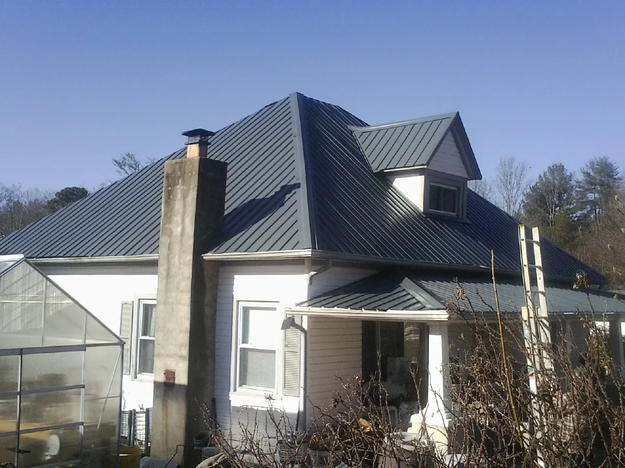 Dark blue standing seam metal roof on a white farmhouse with dormer — Slate & Tile Roof Repair by Roofing Brothers in Lucerne