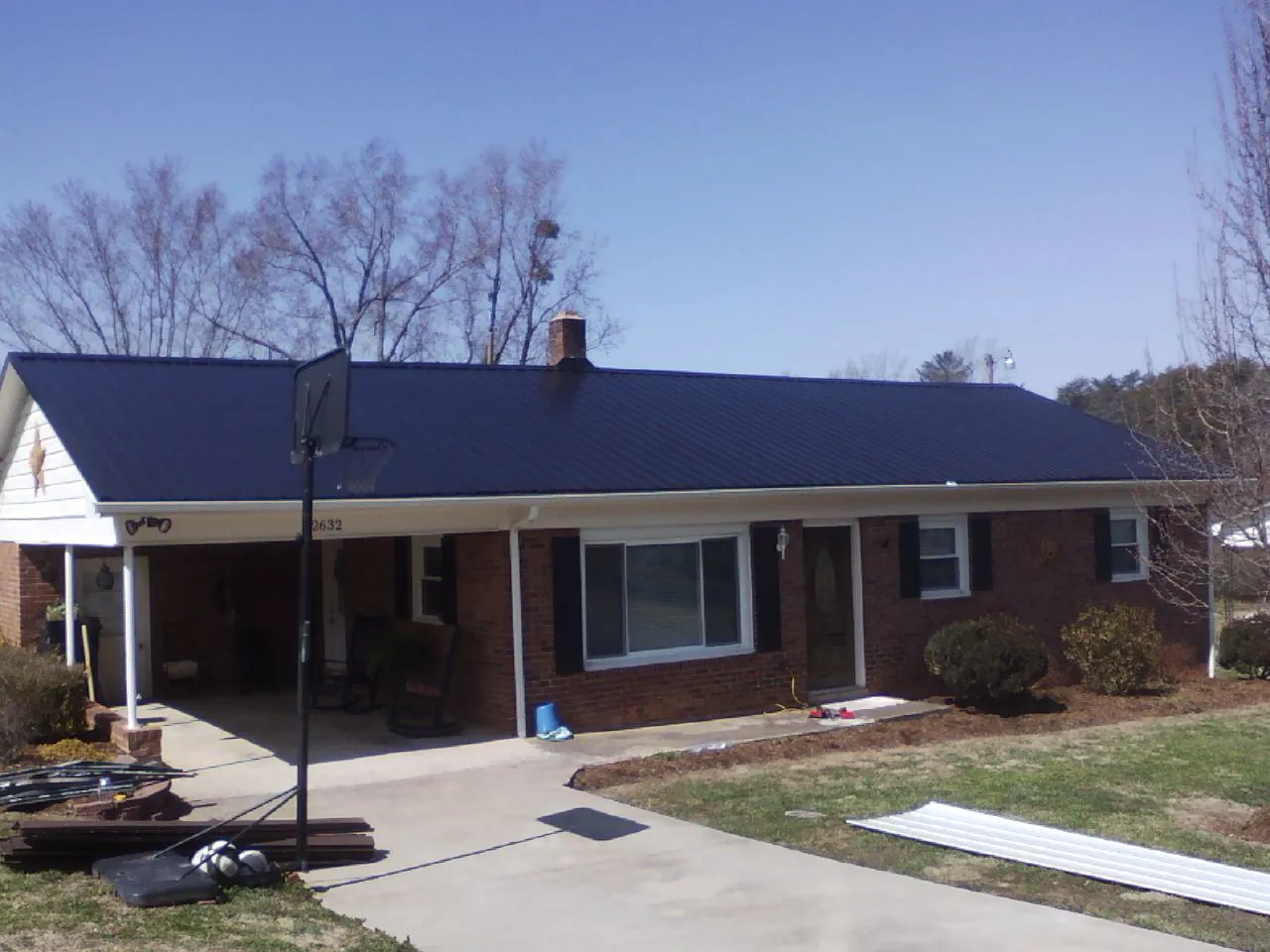 Finished dark blue metal roof on a brick ranch with a carport in Lucerne