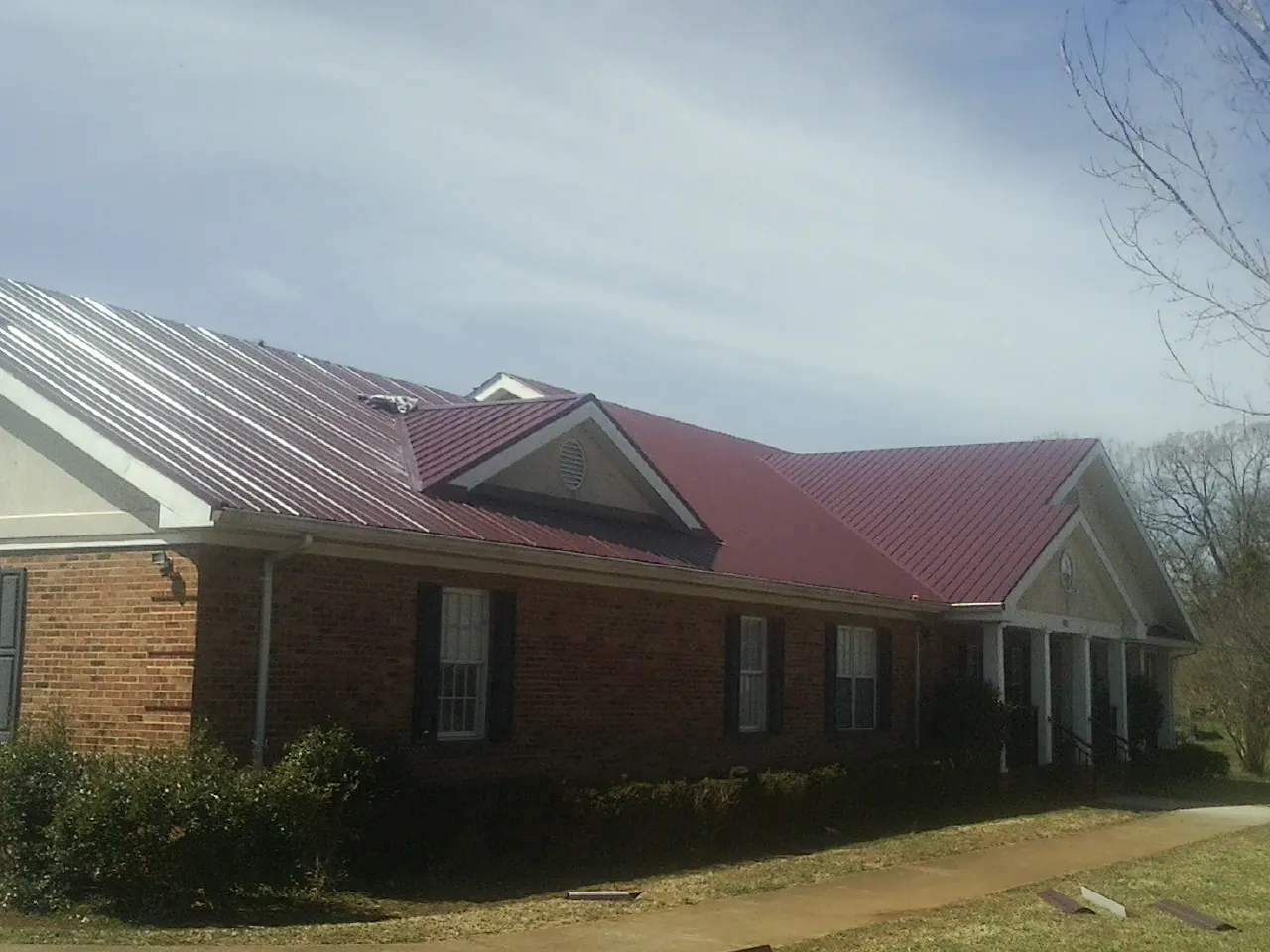 Red metal roof with gabled entries on a long brick building, from a Hail Damage Roof Repair job in Lucerne