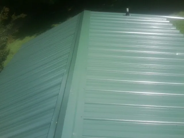 New green metal panels meeting at the ridge of a roof — Flat Roof Repair work by our crew in Lucerne