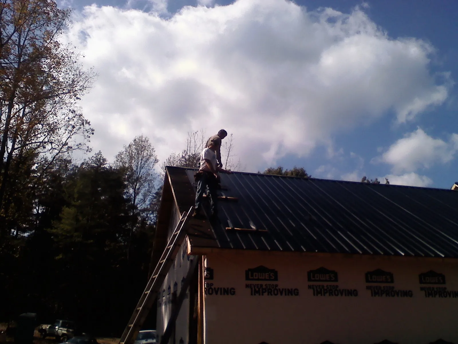 Roofer fastening dark metal panels high against a cloudy sky, from a Roof Inspection job in Lucerne