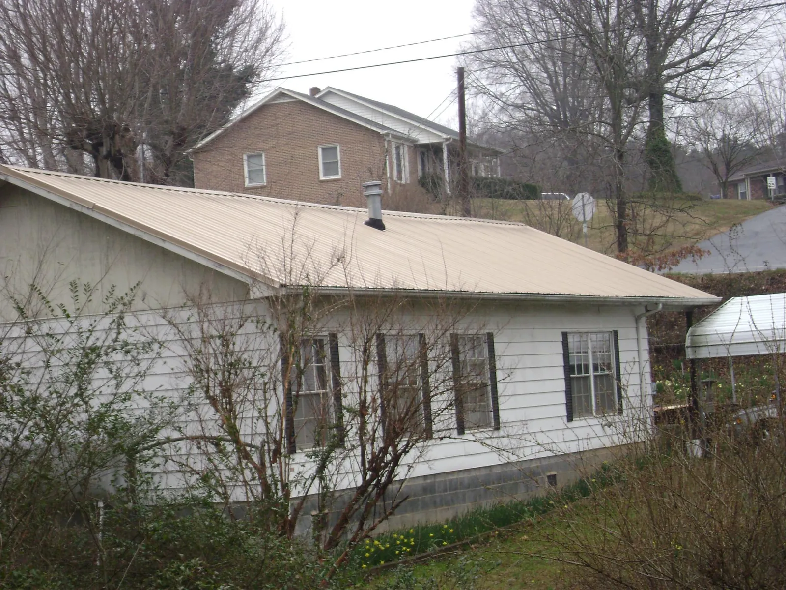 Tan metal roof on a white sided house set into a hillside — Commercial Roofing by Roofing Brothers in Lucerne