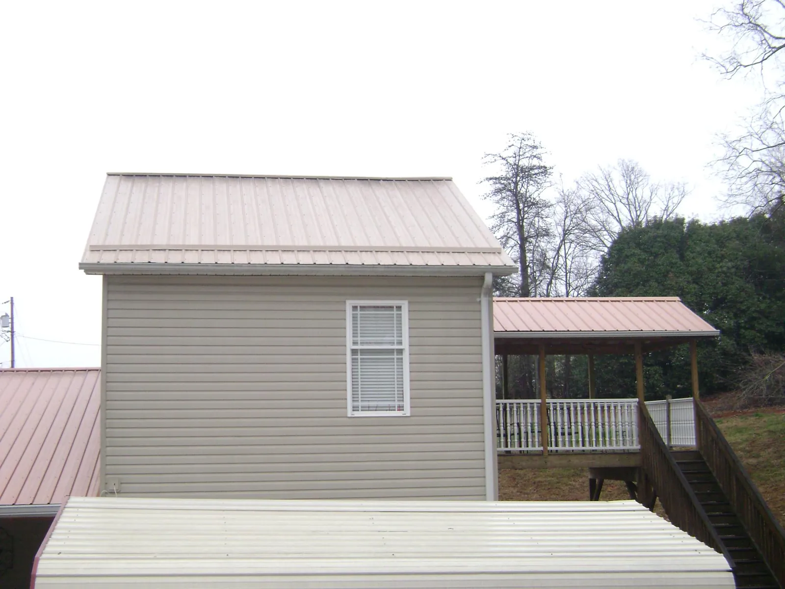 Tan metal roofs on a two story addition and attached porch, from a Roof Replacement job in Lucerne